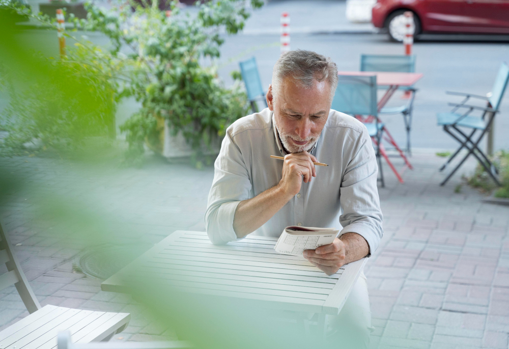 middle aged, smartly dressed man, playing sudoku game, sat at an outside table at a restaurant.